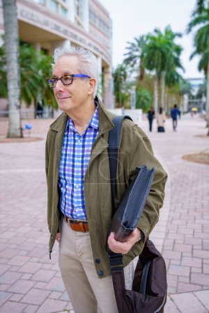 Téléchargez les photos : PHoto of a college professor walking on campus with blurry people in background - en image libre de droit