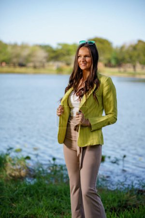 Téléchargez les photos : Belle jeune mannequin féminine posant dans une veste verte dans une nature vue dans le parc - en image libre de droit