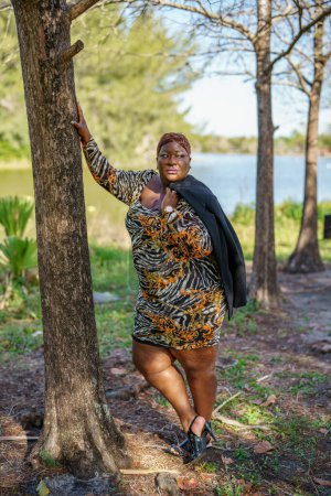 Photo for Beautiful black plus sized model posing by a tree in a tranquil park scene - Royalty Free Image