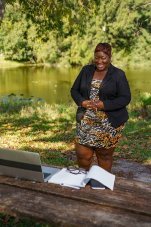 Photo for Plus size CEO businesswoman boss giving a speech in an online group meeting. She is working remotely in the park - Royalty Free Image