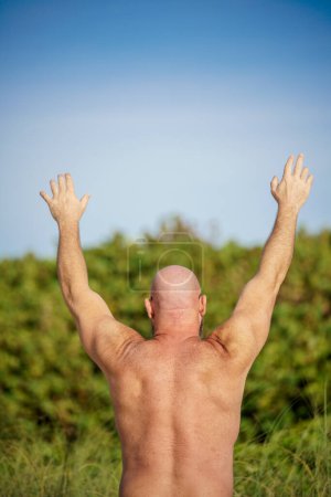Téléchargez les photos : Photo arrière d'un homme sur la plage qui tend la main vers le ciel - en image libre de droit