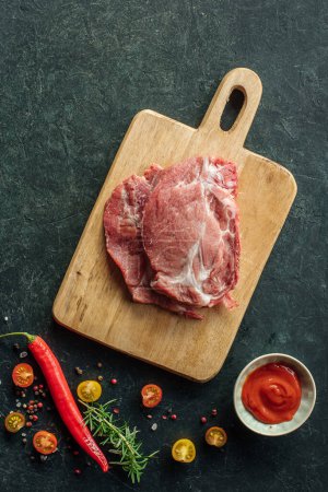 Foto de Carne de cerdo cruda con especias, pimienta picante y salsa de tomate para marinar sobre fondo negro, Vista superior con lugar para texto - Imagen libre de derechos