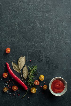 Foto de Fondo vertical con especias, pimienta, salsa de tomate y otros ingredientes sobre un fondo de cocina de piedra negra. Vista superior - Imagen libre de derechos