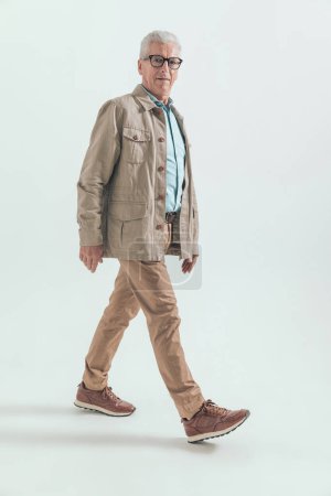 Foto de Viejo hombre casual está caminando de una manera y mirando hacia otro lado en gris tocino estudio - Imagen libre de derechos