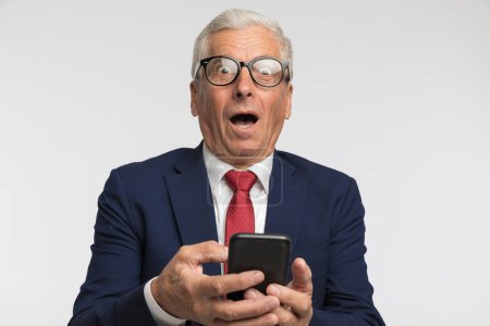 Photo for Businessman feeling shocked after the message he had on his phone against grey studio background - Royalty Free Image