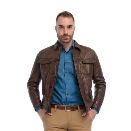 Téléchargez les photos : Casual bearded man in brown leather jacket holding hands in pockets in front of white background in studio - en image libre de droit