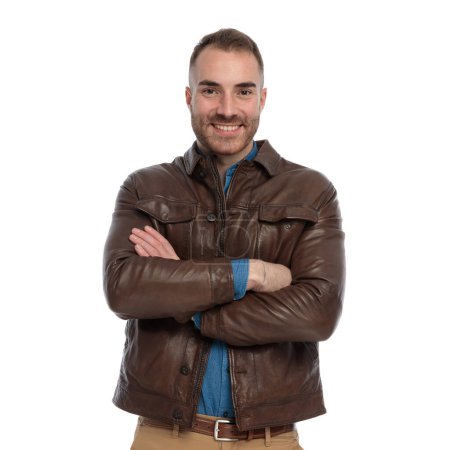 Téléchargez les photos : Excited casual guy in brown leather jacket crossing arms and smiling in front of white background in studio - en image libre de droit