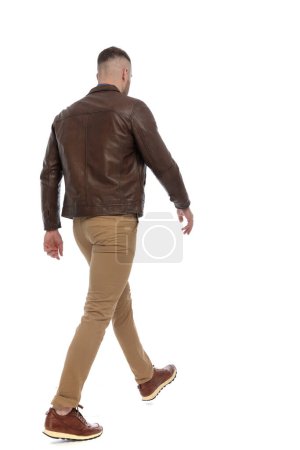 Photo for Rear view of casual man in brown leather jacket walking away in front of white background in studio - Royalty Free Image