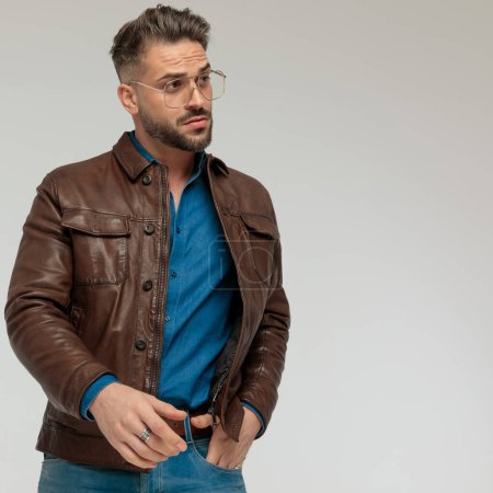 Téléchargez les photos : Portrait of handsome casual man looking to side with one hand in pocket, standing, wearing eyeglasses against gray studio background - en image libre de droit