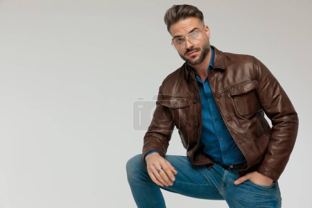 Photo for Portrait of sexy casual man putting a hand in pocket, leaning on one leg, wearing eyeglasses against gray studio background - Royalty Free Image