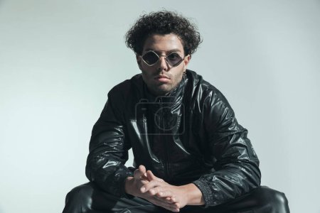 Photo for Handsome turkish man with curly hair in leather jacket posing while touching palms in front of grey background in studio - Royalty Free Image