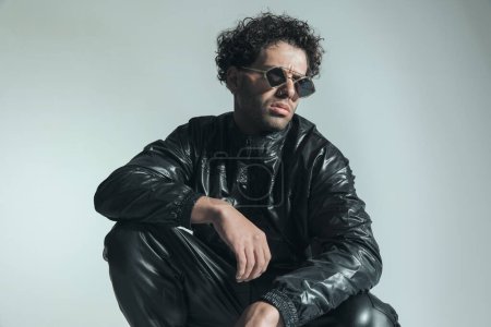 Foto de Fashion lebanese guy in leather jacket wearing sunglasses and looking to side while posing in a cool way on grey background in studio - Imagen libre de derechos
