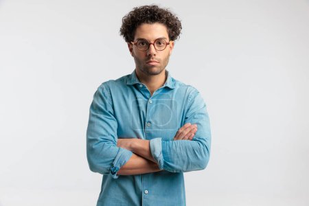 Photo for Portrait of young casual man crossing his arms at chest, standing, wearing a shirt and eyeglasses against gray studio background - Royalty Free Image