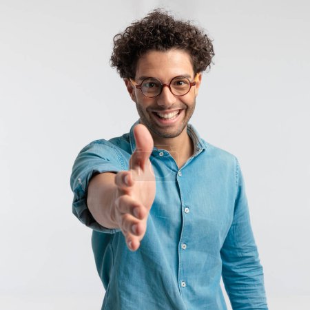 Photo for Portrait of attractive casual man feeling happy to shake hands, standing, wearing a shirt and eyeglasses against gray studio background - Royalty Free Image