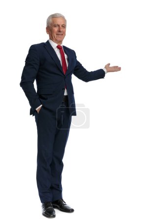 Photo for Full body picture of an old businessman presenting something to the side, putting one hand in pocket - Royalty Free Image
