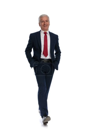 Photo for Full body picture of an Happy old businessman walking towards the camera with his hands in his pockets and a smile on his face - Royalty Free Image