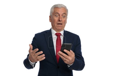 Photo for Old businessman feeling shocked after reading a message on his mobile phone - Royalty Free Image
