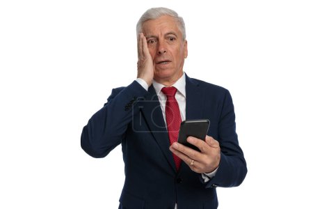 Téléchargez les photos : Old businessman feeling anxious to open he's emails on his mobile phone and slapping his face - en image libre de droit