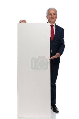 Foto de Full body picture of an old businessman showing us something on a vertical billboard - Imagen libre de derechos