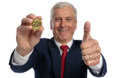 Photo for Old businessman showing a bitcoin and gesturing that's ok to invest in this cryptocoin - Royalty Free Image