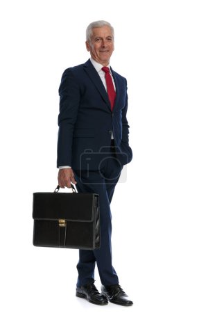 Photo for Full body picture and side view of an old business man crossing legs, putting one hand in pocket and holding a briefcase - Royalty Free Image