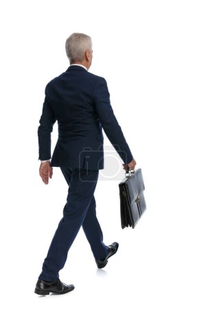 Téléchargez les photos : Full body picture and rear view of an old businessman going to do some business with his briefcase in hand - en image libre de droit