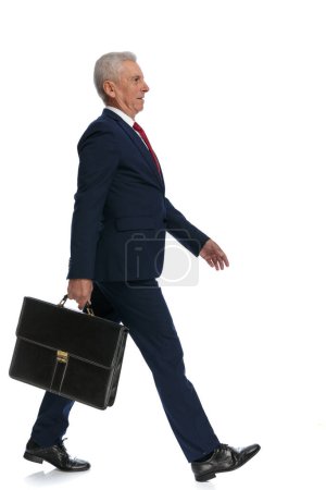 Photo for Full body picture of an old businessman walking to the side on his way and holding a briefcase - Royalty Free Image