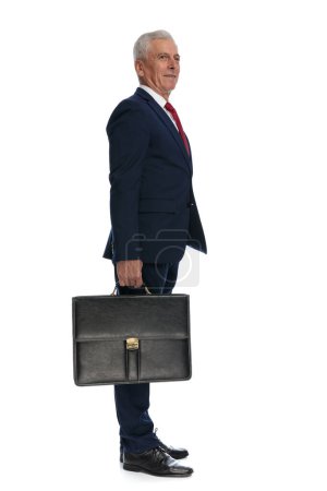 Photo for Full body picture of an old businessman waiting in line while looking away and holding a briefcase - Royalty Free Image