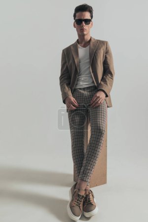 Téléchargez les photos : Fashion man with dark hair laying on a box and posing in front of grey background in studio, full body - en image libre de droit