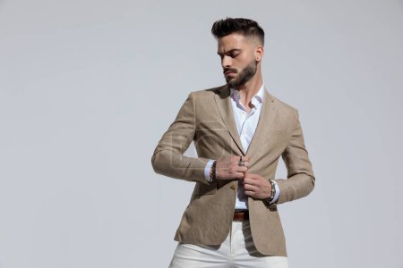 Foto de Portrait of attractive businessman opening his jacket and looking down, standing, against gray studio background - Imagen libre de derechos