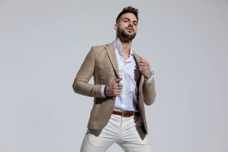 Photo for Portrait of young businessman opening his jacket with attitude, standing, against gray studio background - Royalty Free Image