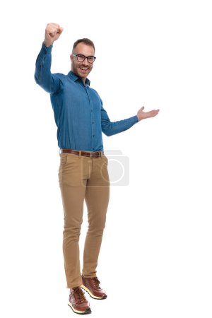 Photo for Full body picture of excited young man holding fist in the air and celebrating the victory,  laughing and walking on white background in studio - Royalty Free Image