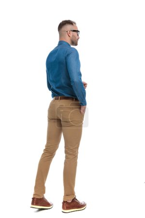 Téléchargez les photos : Full body picture of casual young man walking with hand in pocket in front of white background in studio - en image libre de droit