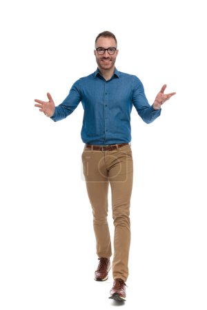 Foto de Happy nerdy man with glasses opening arms and gesturing while walking on white background in studio - Imagen libre de derechos
