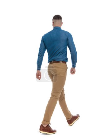 Téléchargez les photos : Back view picture of casual young guy in denim shirt walking in front of white background in studio - en image libre de droit