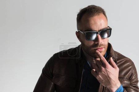 Foto de Portrait of pensive casual guy wearing glasses, touching lips and thinking in front of grey background in studio - Imagen libre de derechos