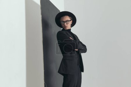 Téléchargez les photos : Portrait of young fashion guy looking over shoulder and posing while crossing arms in front of black board on grey background in studio - en image libre de droit