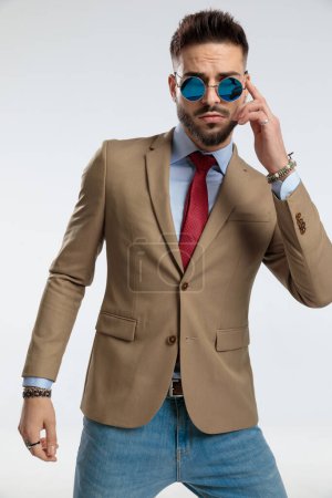 Foto de Portrait of a sexy businessman, standing, fixing sunglasses against gray studio background - Imagen libre de derechos