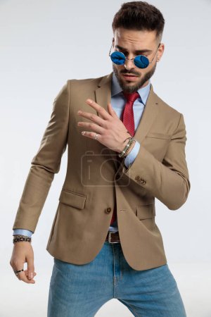 Foto de Portrait of a attractive businessman with a dramatic pose, standing, wearing sunglasses against gray studio background - Imagen libre de derechos
