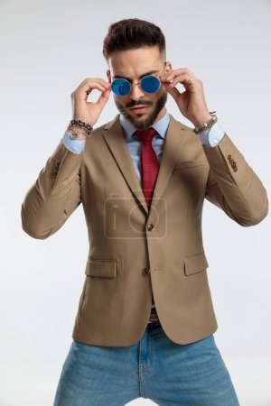 Photo for Portrait of a sexy businessman, standing, fixing sunglasses against gray studio background - Royalty Free Image