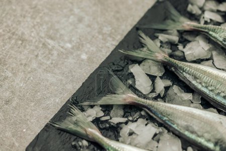 Foto de Concept of freshness illustrated by uncooked white fish tails on chopping board with ice cubes on texture background - Imagen libre de derechos
