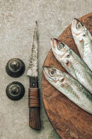 Foto de Table top picture of uncooked fresh seabass on top of wooden cutting board with knife, salt and pepper, concept of cooking healthy meals - Imagen libre de derechos