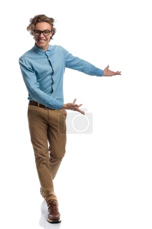 Téléchargez les photos : Full body picture of attractive casual man walking and pointing to the side, standing, wearing eyeglasses against white studio background - en image libre de droit