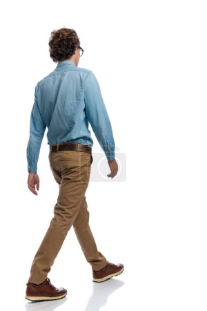 Foto de Imagen de cuerpo completo del joven hombre casual caminando y ocupándose de sus propios asuntos, de pie, usando anteojos contra el fondo blanco del estudio - Imagen libre de derechos