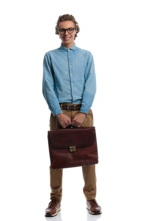 Foto de Full body picture of young casual man posing with briefcase in hands, standing, wearing eyeglasses against white studio background - Imagen libre de derechos