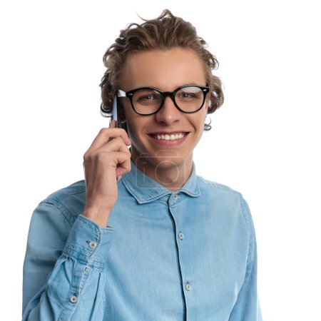 Foto de Closeup picture of sexy casual man talking on the phone while smiling, standing, wearing eyeglasses against white studio background - Imagen libre de derechos