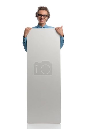 Téléchargez les photos : Full body picture of attractive casual man presenting billboard while smiling, standing, wearing eyeglasses against white studio background - en image libre de droit