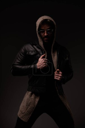 Photo for Mysterious cool man with glasses pulling and adjusting leather jacket on grey background - Royalty Free Image