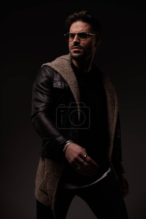 Téléchargez les photos : Portrait d'homme barbu sexy avec des lunettes regardant loin et posant sur fond gris - en image libre de droit