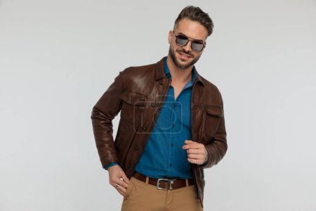 Photo for Portrait of a handsome casual man putting one hand in pocket, standing, wearing sunglasses against gray studio background - Royalty Free Image